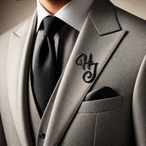 May include: A light gray suit with a black tie and pocket square. A black monogram pin with the letters "HJ" is pinned to the lapel. The suit has a white collared shirt underneath.