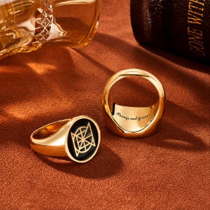 May include: Two gold-toned rings with a polished finish. One ring features a circular black inlay with a geometric gold symbol. The other ring is positioned to show the interior engraving which reads Always and forever in a cursive script font.