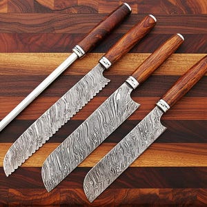 May include: A set of four kitchen knives and a sharpening steel arranged on a wooden cutting board. The knives have patterned blades and wooden handles with silver accents. The sharpening steel is silver with a wooden handle.
