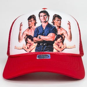 May include: Red and white trucker hat featuring a graphic of a man in a blue shirt and jeans, surrounded by images of the same man. The hat has a red brim and a white mesh back.