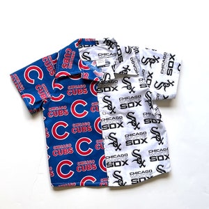 May include: A short-sleeved button-down shirt featuring a split design. One side displays a blue pattern with "CHICAGO CUBS" in red and white. The other side showcases a white pattern with "CHICAGO WHITE SOX" in black.