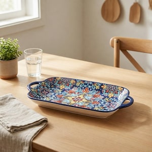 Peut inclure: Un plateau de service rectangulaire en céramique doté de deux poignées, orné d'un motif floral et géométrique multicolore aux tons bleu profond, jaune, rouge et blanc. Le plateau présente une finition brillante et un bord bleu foncé.