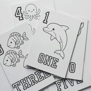 Peut inclure: Cartes mémoire blanches avec des illustrations noires de créatures marines et de chiffres. Les cartes présentent un dauphin, un poisson et une pieuvre. Les chiffres et les mots comme "ONE", "THREE", "FOUR" et "FIVE" sont imprimés sur les cartes.
