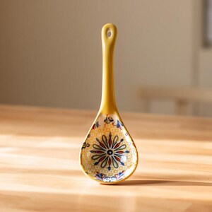Peut inclure: Une cuillère en céramique jaune avec un motif floral décoratif. La cuillère a un long manche avec un trou pour l'accrocher et une cuillère en forme de bol. Le motif floral comprend des accents rouges, bleus et jaunes.