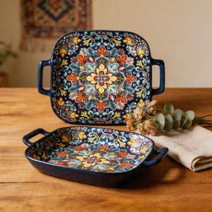 Peut inclure: Deux plats de service en céramique avec un fond bleu foncé et un motif floral coloré. Les plats ont des poignées et sont carrés et rectangulaires. Le motif floral comprend des éléments jaunes, oranges et bleus.