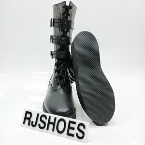 May include: Black leather combat boots with multiple buckles and laces. The boots have a textured sole and are displayed with the sole facing up. The text "RJSHOES" is visible on a white sign.