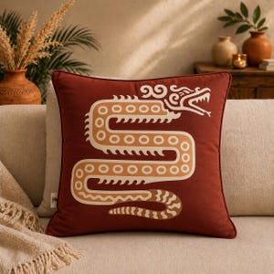 May include: A square, rust-colored decorative pillow featuring a stylized serpent design in cream and tan. The serpent is centered on the pillow, with a detailed head and body. The pillow has a solid rust border.