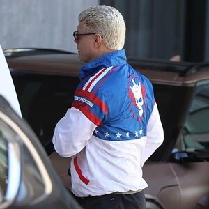 May include: A blue, red, and white athletic jacket with a skull graphic on the back. The jacket has a star pattern and the text "BODYSHOOTER" on the front. The jacket is worn by a person with light-colored hair and sunglasses.