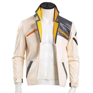 Op de afbeelding: Crèmekleurige jas met zwarte en grijze accenten. De jas heeft oranje ritsen, een geel honingraatpatroon op de kraag en zwarte afwerking. De jas wordt op een mannequin gepresenteerd.