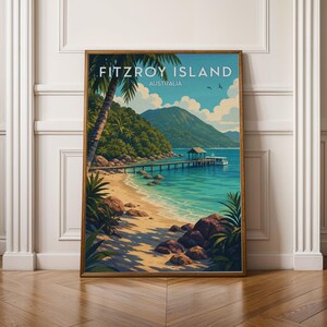 May include: A framed vertical art print featuring a tropical beach scene with the text FITZROY ISLAND AUSTRALIA. The image displays a sandy shore, turquoise water, a wooden pier with a small boat, lush green hills, and a blue sky with clouds.