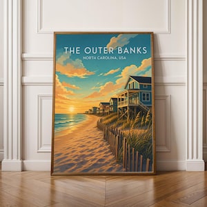 May include: A framed print featuring a beach scene from The Outer Banks, North Carolina. The artwork depicts a sunset over the ocean, with colorful houses along the shore, a wooden fence, and text that reads "THE OUTER BANKS NORTH CAROLINA, USA."