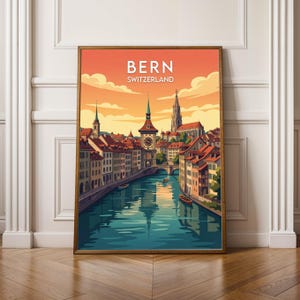 May include: A framed art print of Bern, Switzerland, featuring a vibrant illustration of the city's architecture. The artwork showcases a river, buildings with red roofs, and a clock tower under an orange and yellow sky. The text "BERN SWITZERLAND" is at the top.