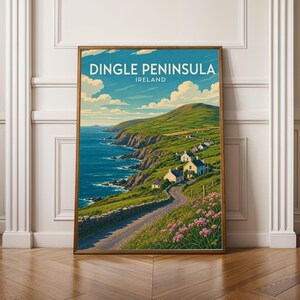 May include: A framed travel poster featuring the Dingle Peninsula in Ireland. The illustration depicts a winding road along a green coastal cliffside, small houses, blue ocean waters, and pink wildflowers under a blue sky with white clouds.