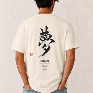May include: An off-white short-sleeve t-shirt featuring a large black Japanese kanji character for dream on the back. Below the character is the English word DREAM, the romanized word Yume, and the Japanese hiragana characters for dream.
