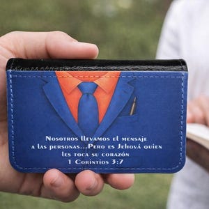 May include: A blue wallet featuring a graphic of a suit with an orange shirt and blue tie. A pen is in the pocket. The wallet has text in Spanish: "Nosotros llevamos el mensaje a las personas...Pero es Jehová quien les toca su corazón 1 Corintios 3:7."