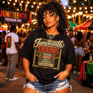 May include: A black short-sleeve t-shirt featuring a graphic with the text Juneteenth 1865 and the words Freedom, Legacy, Unity, Strength, and Heritage. The design includes gold, red, and green accents with a rope-style border on a black background.