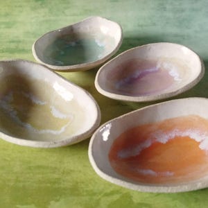 May include: Four handmade ceramic dishes with organic shapes and a glossy finish. Each dish features a unique colour palette, including shades of green, purple, yellow, and orange, with white accents. These decorative dishes are perfect for serving small portions.