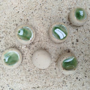 Peut inclure: Ensemble de pièces en céramique faites à la main. Les pièces sont de couleur beige clair avec un centre vert brillant. Certaines pièces ont de petites mouchetures marron. Une pièce est un ovale beige uni.