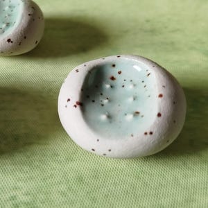 Könnte beinhalten: Nahaufnahme von drei kleinen, gesprenkelten Keramikschalen. Die Schalen sind weiß mit hellblauem Innenraum und braunen Sprenkeln. Die Schalen stehen auf einer hellgrünen Oberfläche.