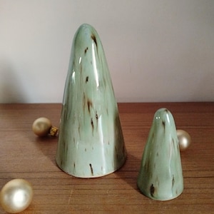 May include: Two cone-shaped ceramic sculptures with a glossy light green glaze and dark brown vertical streaks. The larger cone stands to the left, while the smaller cone is positioned to the right, accompanied by three small, round, metallic gold spheres.