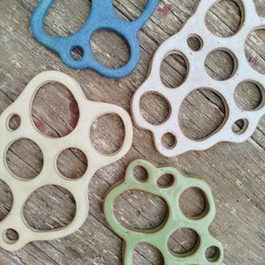 Peut inclure: Quatre dessous de verre en céramique bleus, blancs, crème et verts. Chaque dessous de verre a une forme organique unique avec de multiples découpes circulaires. Les dessous de verre sont disposés sur une surface en bois vieilli.