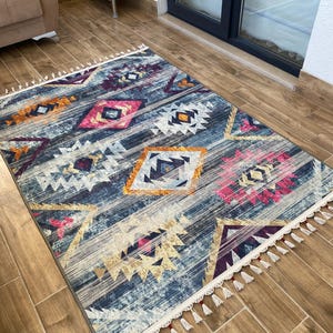 May include: A rectangular area rug with a geometric pattern in shades of blue, pink, orange, and white. The rug has a distressed look with a fringe border. The design features diamond and triangle shapes.