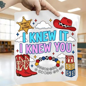K&ouml;nnte beinhalten: Ein wei&szlig;es Stofftuch mit einem bunten Grafikdruck und dem Text I KNEW IT I KNEW YOU. Das Design zeigt einen gelben Sheriffstern, einen roten Cowboyhut, rote Cowboystiefel, ein Perlenarmband mit dem Text you've got a friend in me sowie gestapelte Buchstabenw&uuml;rfel.
