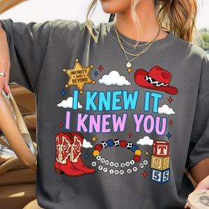 K&ouml;nnte beinhalten: Ein anthrazitfarbenes T-Shirt mit einem Grafikdruck, der einen gelben Sheriffstern mit der Aufschrift INFINITY AND BEYOND, einen roten Cowboyhut, rote Cowboystiefel, ein Perlenarmband mit dem Text YOU'VE GOT A FRIEN ON ME und drei Bl&ouml;cke zeigt.