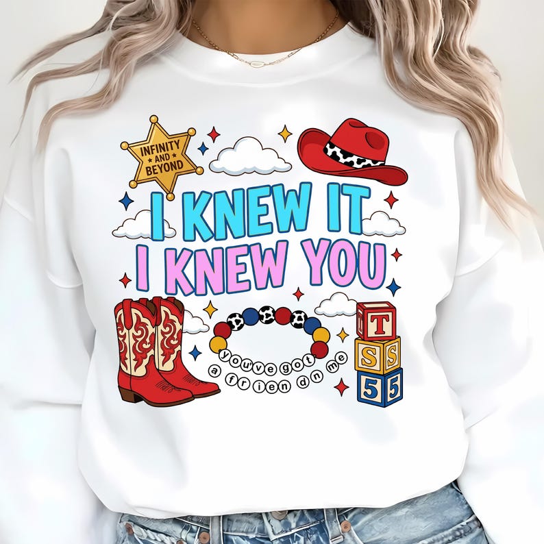 K&ouml;nnte beinhalten: Ein wei&szlig;es Sweatshirt mit einem Grafikdruck, der einen gelben Sheriffstern mit der Aufschrift Infinity and Beyond, einen roten Cowboyhut, rote Cowboystiefel, ein buntes Perlenarmband mit dem Text you've got a friend in me und drei Spielw&uuml;rfel zeigt.