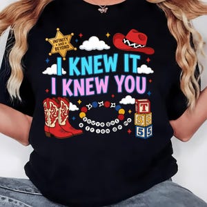 K&ouml;nnte beinhalten: Ein schwarzes T-Shirt mit einem Grafikdruck, der einen gelben Sheriffstern mit der Aufschrift Infinity and Beyond, einen roten Cowboyhut, rote Cowboystiefel, ein Perlenarmband mit dem Text You've Got A Friend In Me und Bl&ouml;cke mit T, S, 5 zeigt.