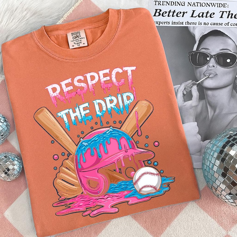 May include: Orange t-shirt with the text "RESPECT THE DRIP" in white, pink, and blue. The graphic features a baseball helmet, baseball bat, and baseball with a dripping design. The shirt is a crew neck.