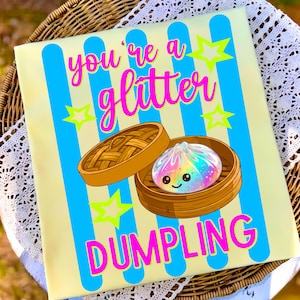 May include: A light yellow canvas with blue vertical stripes and the words "you're a glitter dumpling" in pink. A cartoon dumpling with a rainbow glitter effect sits in a bamboo steamer, with neon green stars.