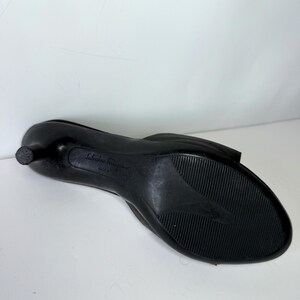 May include: Black Salvatore Ferragamo low-heeled shoe. The shoe has a rounded toe and a small heel. The sole is textured with a ridged pattern. The brand name is visible on the sole.