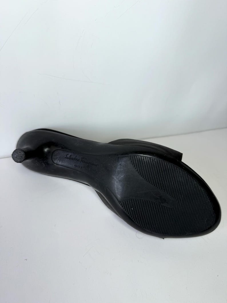May include: Black Salvatore Ferragamo low-heeled shoe. The shoe has a rounded toe and a small heel. The sole is textured with a ridged pattern. The brand name is visible on the sole.