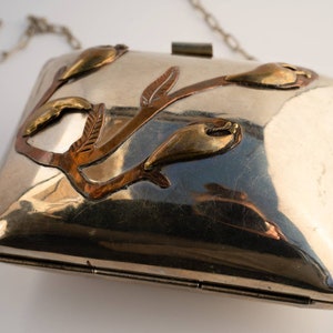 May include: A silver metal clutch bag with a chain strap. The bag features a floral design with copper and brass accents.