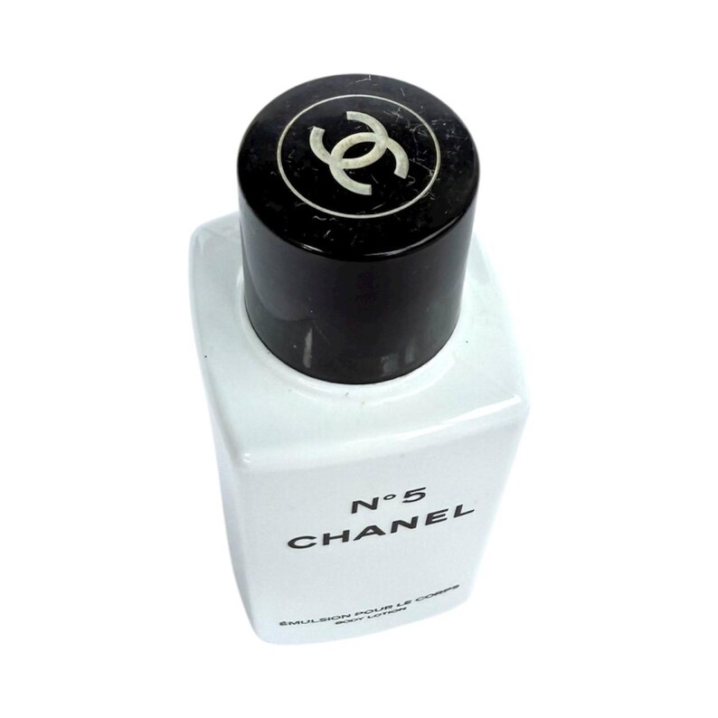 May include: A white rectangular bottle of Chanel No. 5 body lotion with a black cap. The cap features a white interlocking double-C logo. The product name and brand are printed in black on the front of the bottle.