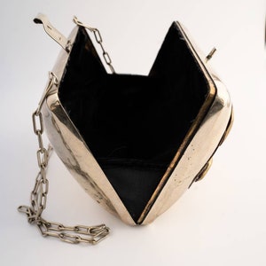May include: A silver metal clutch bag with a chain strap and a black velvet lining. The bag is open and the lining is visible.