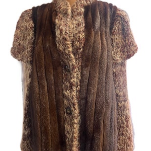 Könnte beinhalten: Eine braune Pelz-Weste mit einem gestrickten braunen und cremefarbenen Cardigan. Die Weste hat einen Knopfverschluss und der Cardigan hat kurze Ärmel.