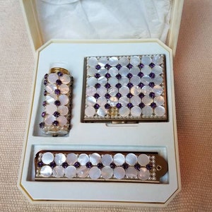 May include: A white vanity set with a compact mirror, a small bottle, and a comb. All three items are decorated with a pattern of white circles with purple accents.
