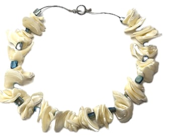 Puede incluir: Un collar de conchas blancas con cuentas de vidrio azul. El collar está hecho de materiales naturales y tiene un diseño simple y elegante.