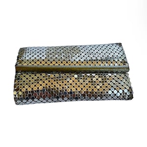 May include: Silver mesh clutch with a rectangular shape. The clutch has a metallic sheen and a clasp closure. The mesh is made of small, circular pieces. The clutch is a vintage accessory.