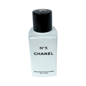 May include: A small, rectangular bottle of Chanel No. 5 body lotion. The bottle is clear with a black cap and features the brand name and product details in black lettering. The lotion is labeled "&Eacute;mulsion pour le corps / Body Lotion."