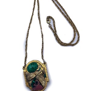 May include: A gold chain necklace with a large oval pendant featuring a green, pink, and white stone design.