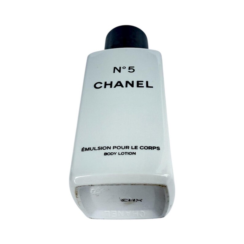 May include: White body lotion bottle with a black cap. The bottle has the text "N&deg;5 CHANEL" and "&Eacute;MULSION POUR LE CORPS BODY LOTION" printed on it. The bottle is rectangular with rounded edges.