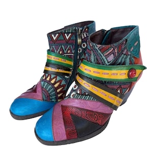 May include: A pair of colorful ankle boots with a variety of patterns and textures. The boots feature a blue toe, a zipper, and straps in multiple colors, including green, yellow, and red. The boots have a heel.