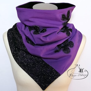 Peut inclure: Écharpe mauve avec des appliqués floraux noirs et une bordure noire scintillante. L'écharpe est drapée sur un mannequin, mettant en valeur son design et sa texture. Le texte "Darja-Ustrzja" est visible sur le côté.