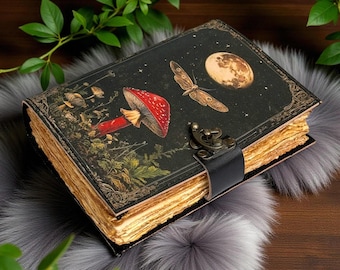 Peut inclure: Un journal de style vintage avec une couverture noire ornée d'un champignon rouge, d'un papillon de nuit et d'un motif de lune. Le journal a une fermeture à lanière en cuir et des pages vieillies.