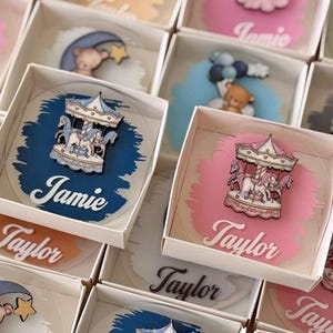 May include: A collection of personalised gifts in small white boxes. Each gift features a unique design, including a carousel, teddy bear, lion, and bunny, set against colourful backgrounds. Names like "Jamie" and "Taylor" are displayed.