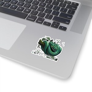 May include: A die-cut sticker featuring a coiled green snake resting on a brown tree branch, surrounded by dark green monstera leaves. The text "SNAKE MORGEN" is printed in white capital letters at the bottom of the sticker design.