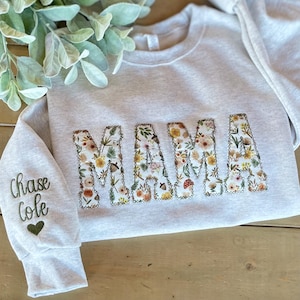 May include: A light gray sweatshirt with the word "MAMA" embroidered in floral fabric. The sleeve features the name "Chase Cole" embroidered in green, with a green heart below.